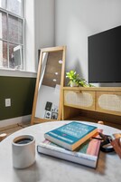 Una habitación con un armario de madera, un televisor de pantalla plana, un espejo y una mesa con libros y una taza de café.