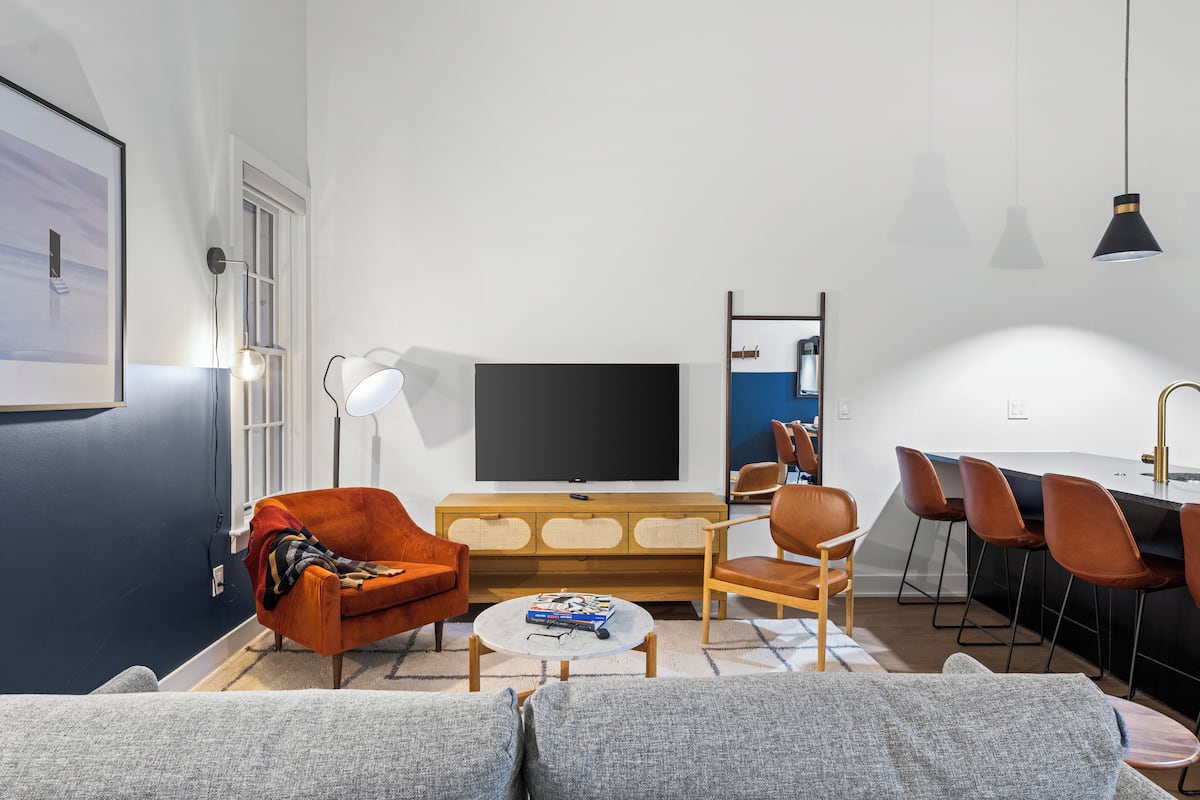 Una sala moderna con un televisor de pantalla plana grande, un sofá, una mesa de centro y un comedor con taburetes de bar.