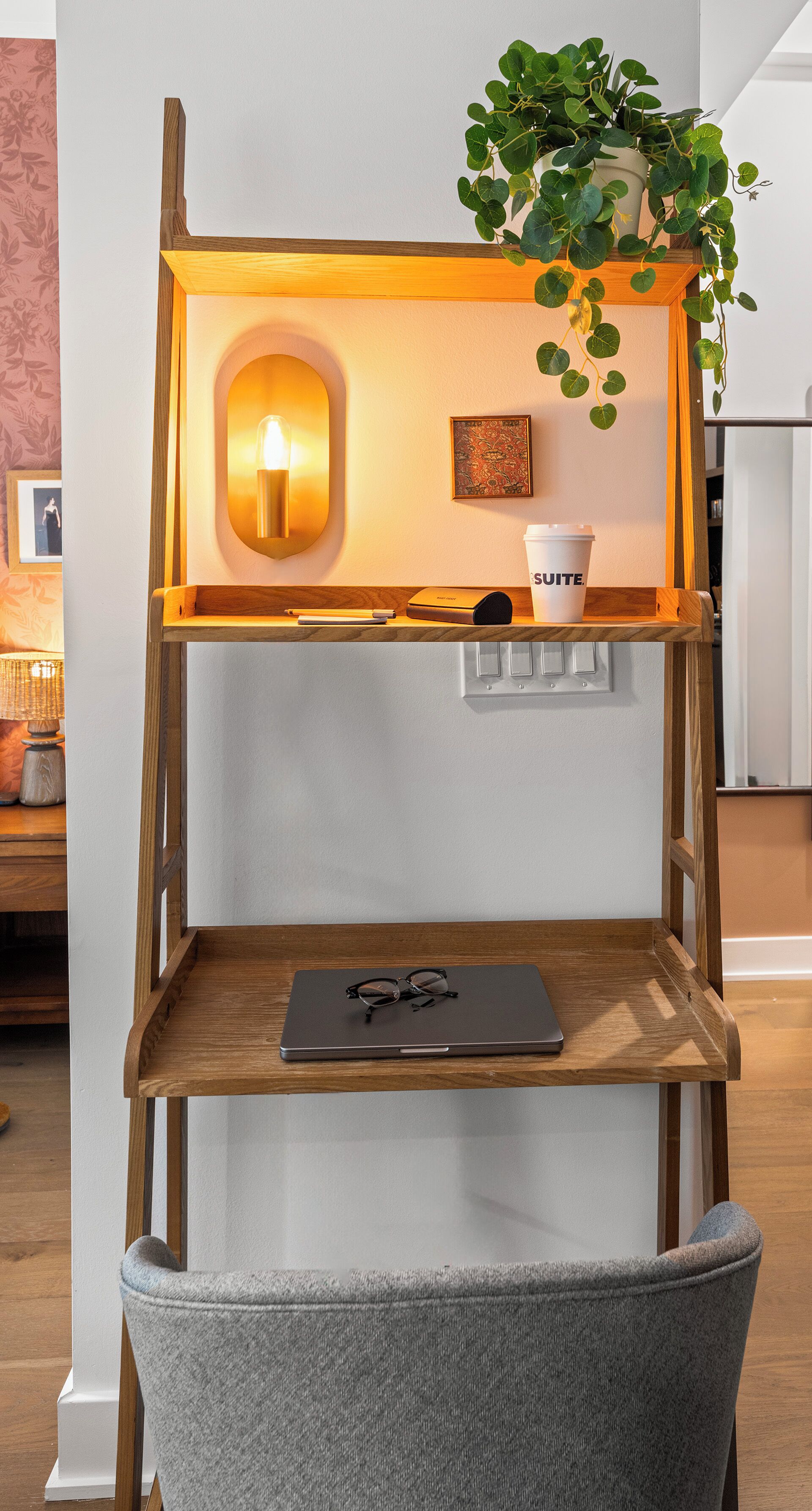 A wooden shelf unit with a laptop, glasses, a cup, and a plant.
