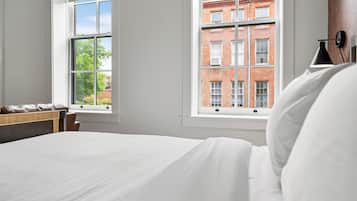 A bedroom with a large bed, two windows, and a view of a brick building.