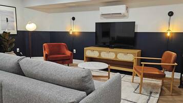 Una sala de estar moderna con un sofá gris, sillas rojas y marrones, una mesa de centro de madera, un televisor de pantalla plana e iluminación empotrada.