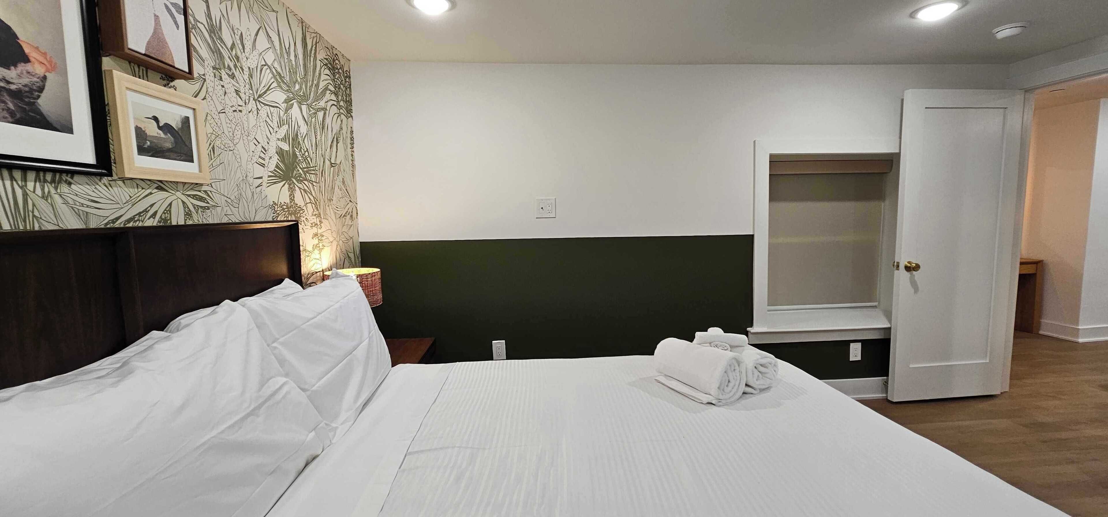 A hotel room with a bed, a nightstand, a lamp, a wardrobe, and a door.