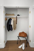 Un placard avec des vêtements suspendus et un sac posé sur un tabouret.