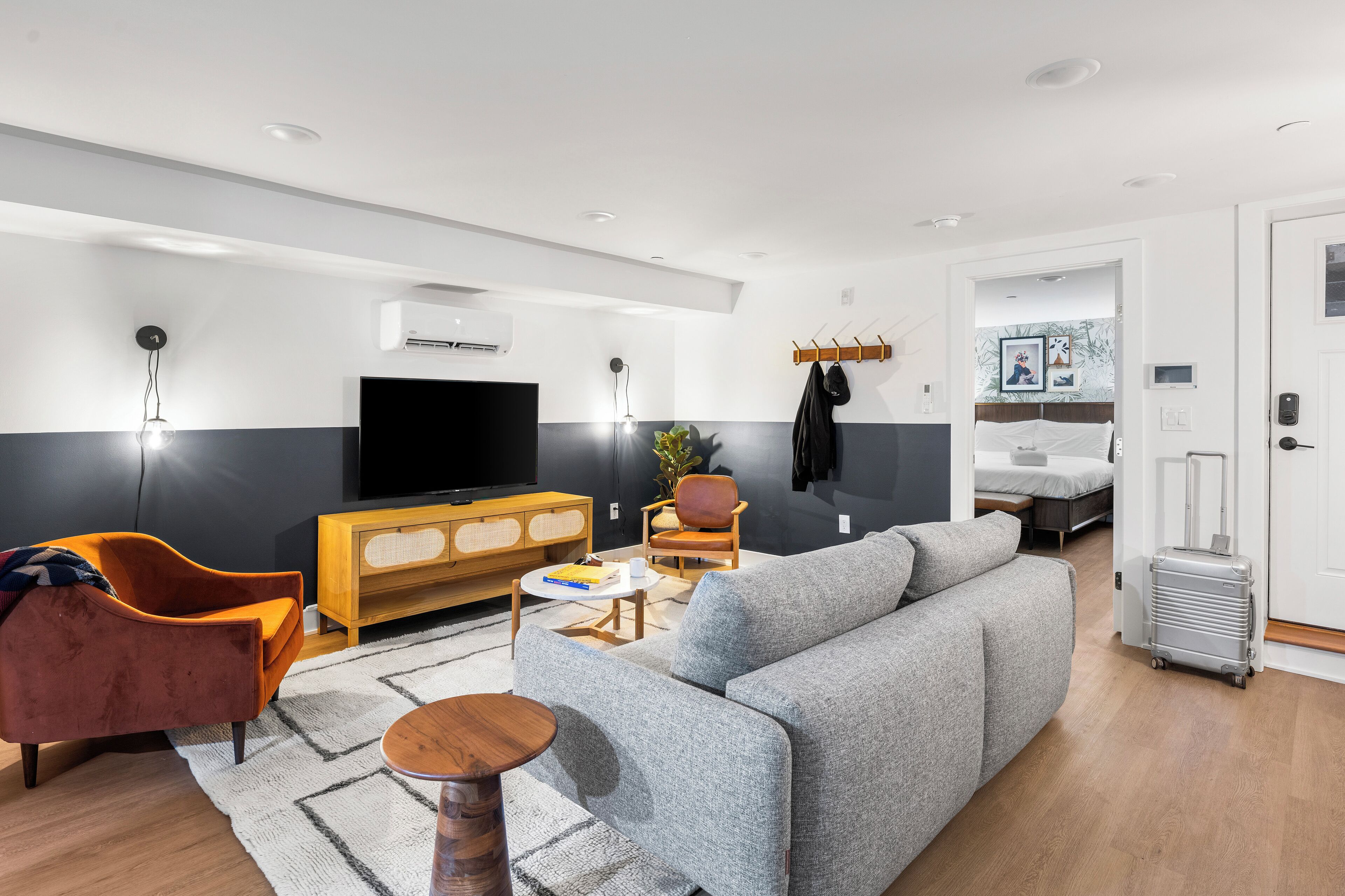 A modern living room with a grey sofa, orange armchair, wooden sideboard, flat-screen TV, and a small table with a plant.