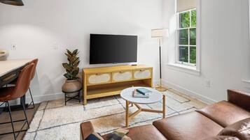 A modern living room with a flat-screen TV, wooden console, leather sofa, and a dining area with chairs and a table.