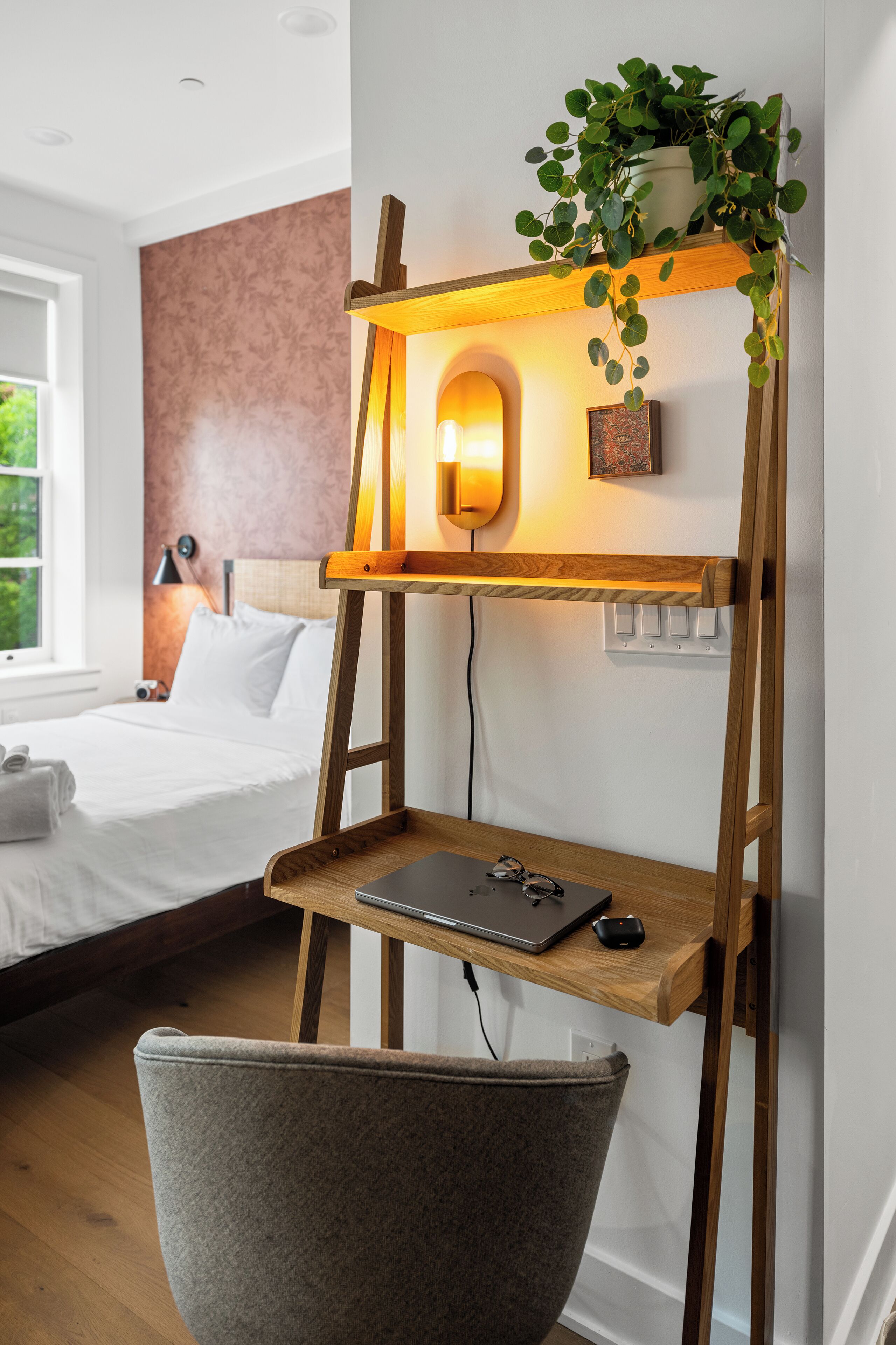 Un dormitorio moderno con cama, lámpara de noche y un escritorio de madera con una computadora portátil y un ratón.