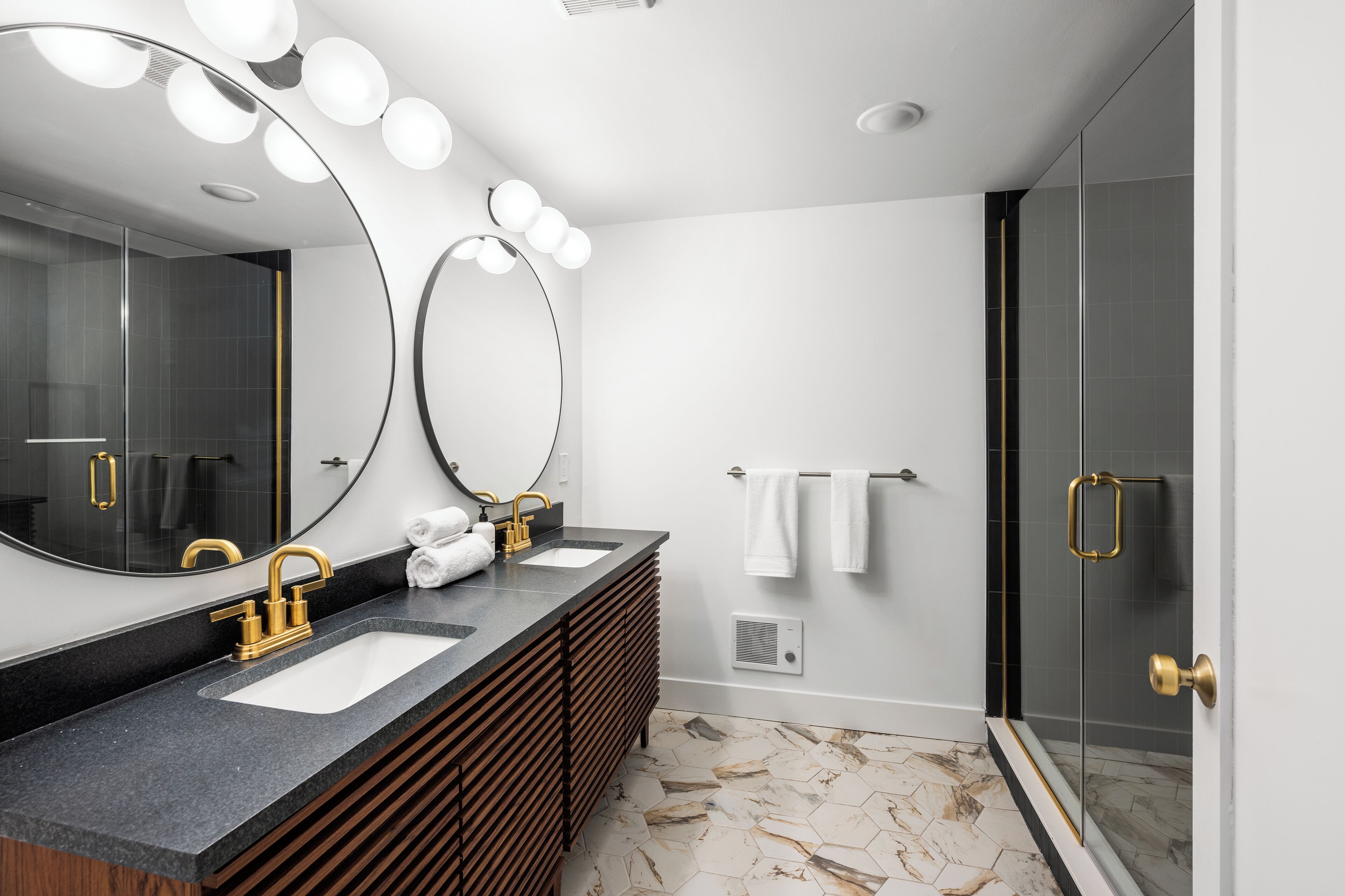 A modern bathroom with two sinks, a large mirror, and a glass shower enclosure.