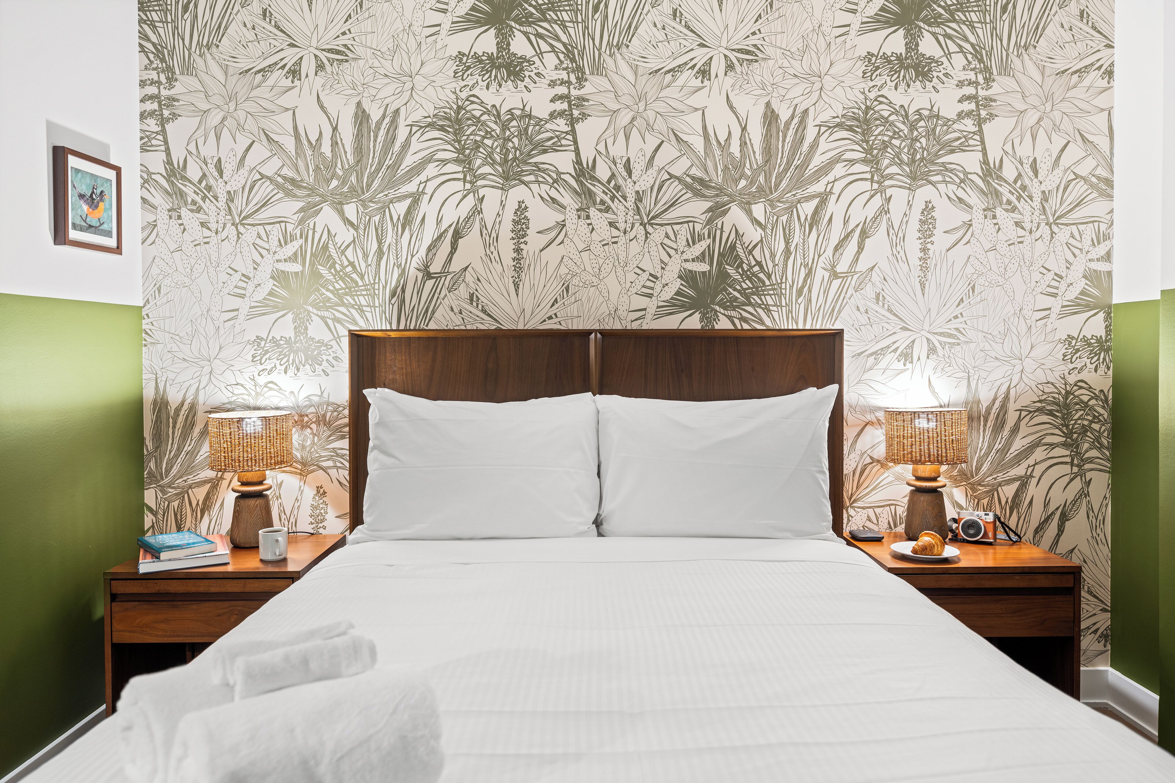 A neatly made bed with white linens, flanked by two wooden nightstands with lamps and a camera.