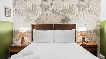 A neatly made bed with white linens, flanked by two wooden nightstands with lamps and a camera.