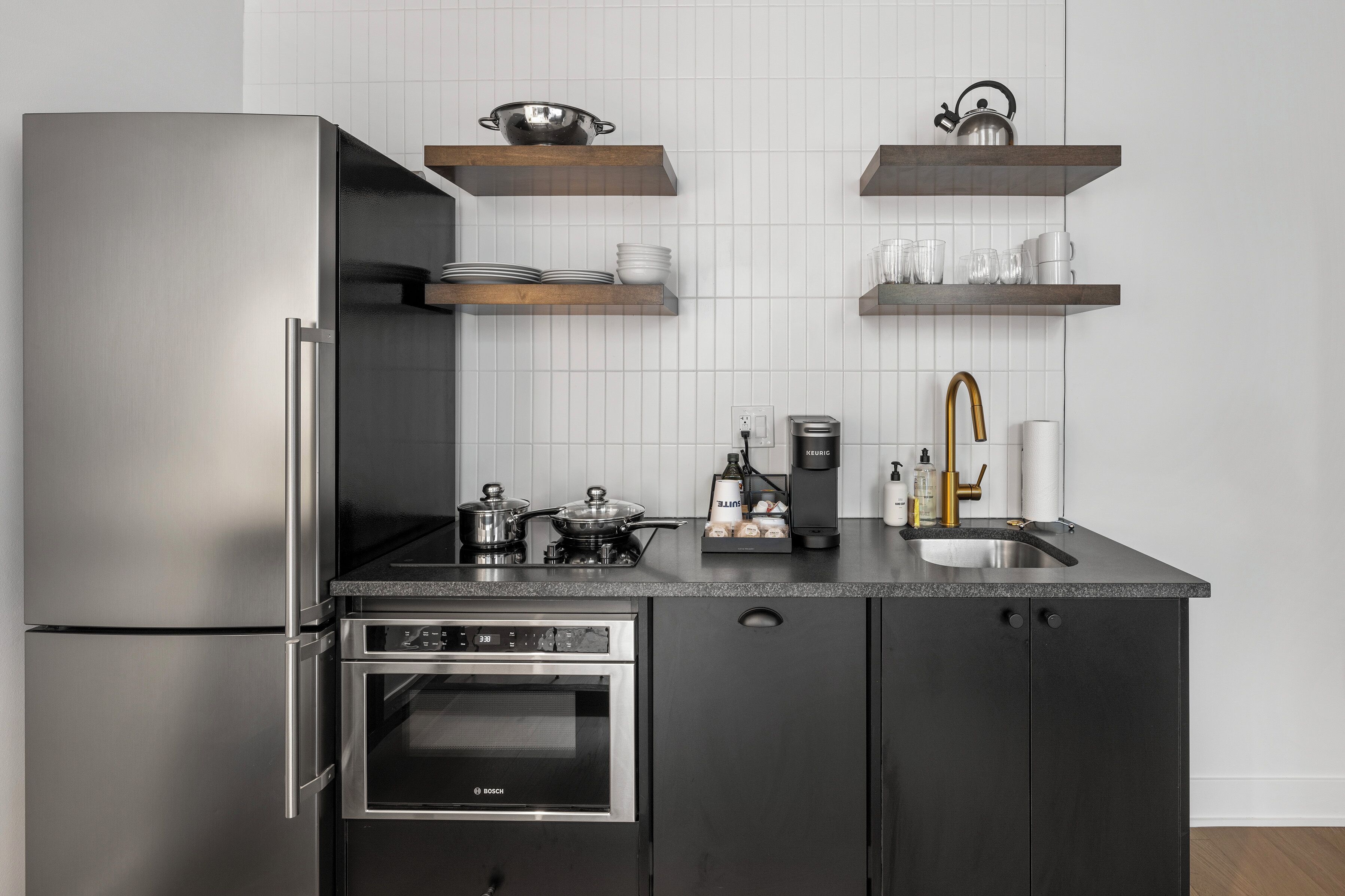 Eine kompakte Küche mit einem Edelstahl-Kühlschrank, einem Einbauofen, einer Kaffeemaschine und Holzregalen über der Arbeitsfläche.