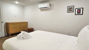 Un dormitorio con cama, cómoda de madera, aire acondicionado y dos cuadros en la pared.