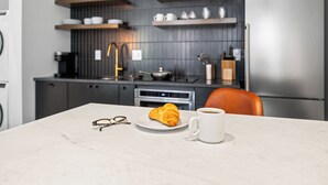 Une cuisine moderne avec un plan de travail en marbre, un croissant, une tasse de café et une paire de lunettes.