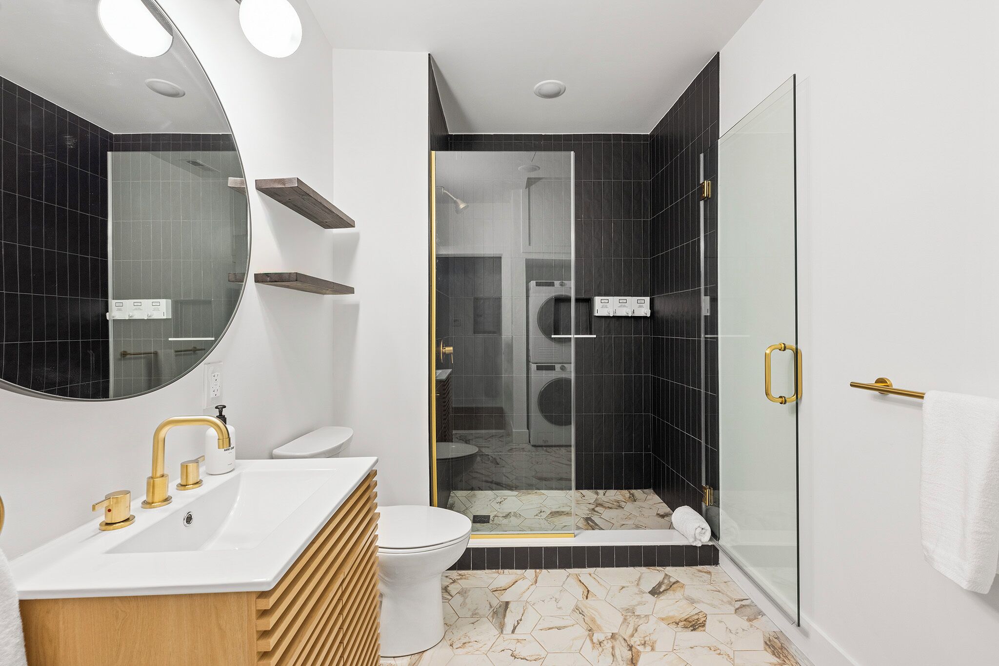 Ein modernes Badezimmer mit einem weißen Waschbecken, goldenen Armaturen, einer Duschkabine aus Glas und einem Boden aus Marmorplatten.