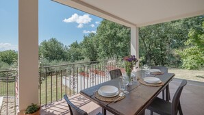 Une terrasse extérieure avec une table dressée pour le repas, entourée de chaises, et donnant sur un jardin luxuriant.
