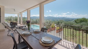 Un coin repas avec une table dressée pour quatre personnes, offrant une vue panoramique sur un paysage magnifique, avec des montagnes et des arbres.