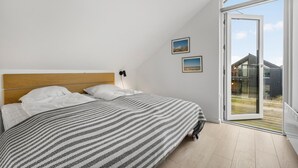 Un dormitorio con una cama grande, un cabecero de madera, vista a través de un ventanal corredero y dos cuadros en la pared.