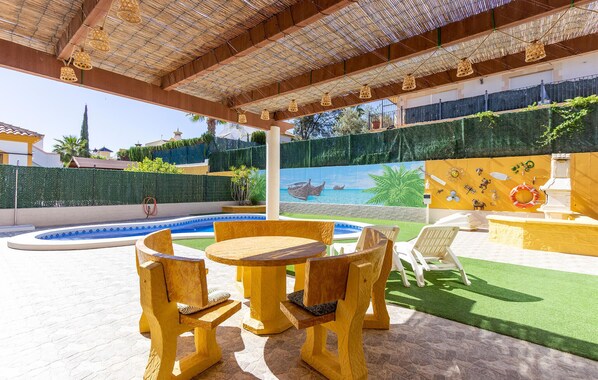 Un espace extérieur abrité comprenant une piscine, des meubles en bois et une fresque murale.