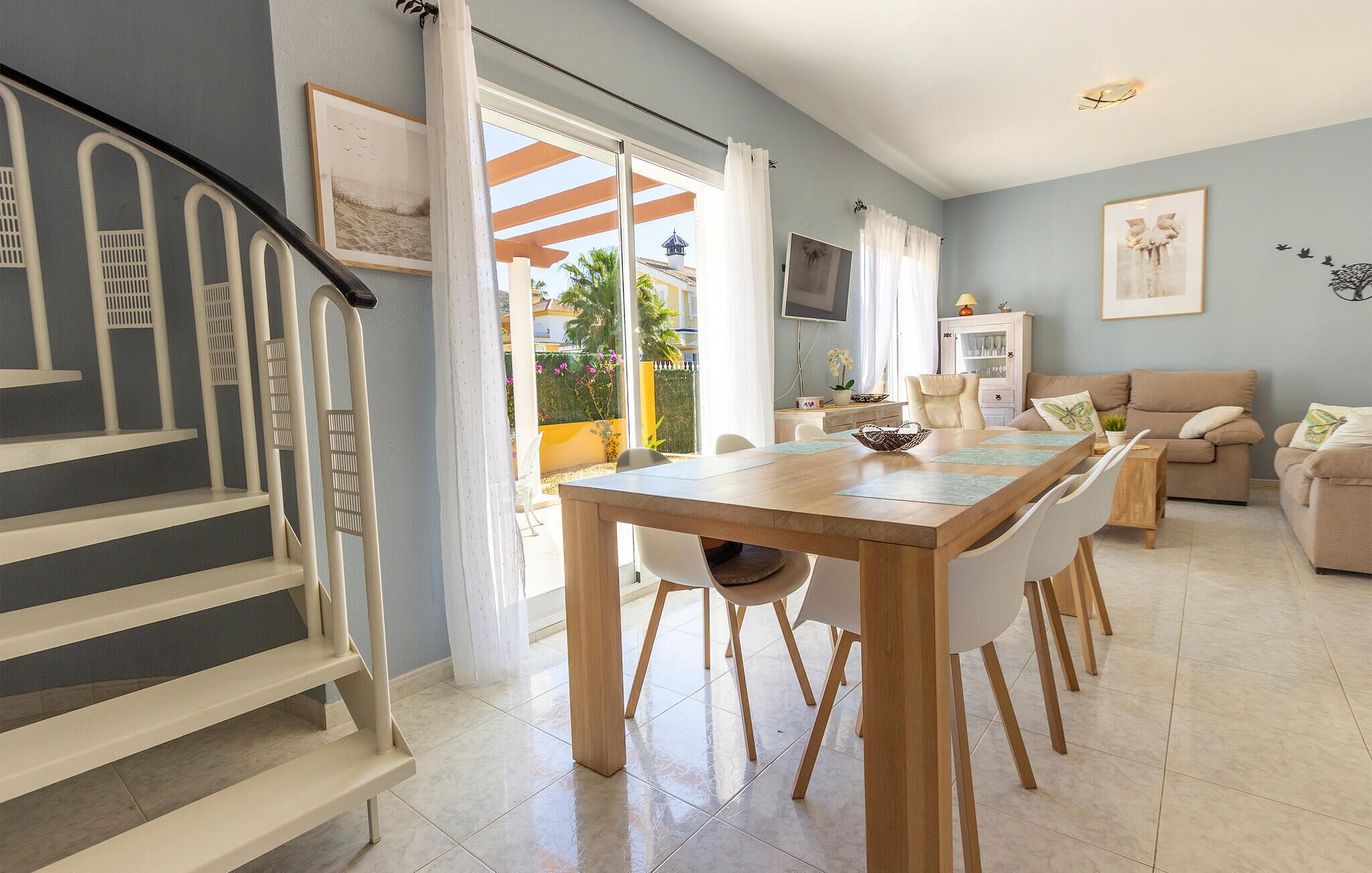 A modern living room with a dining area, a staircase, and a view of the outside.