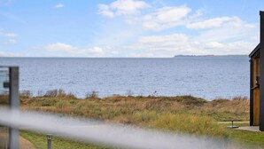 Une vue d’une zone côtière avec une étendue d’eau, un terrain herbeux et un bâtiment en bois.