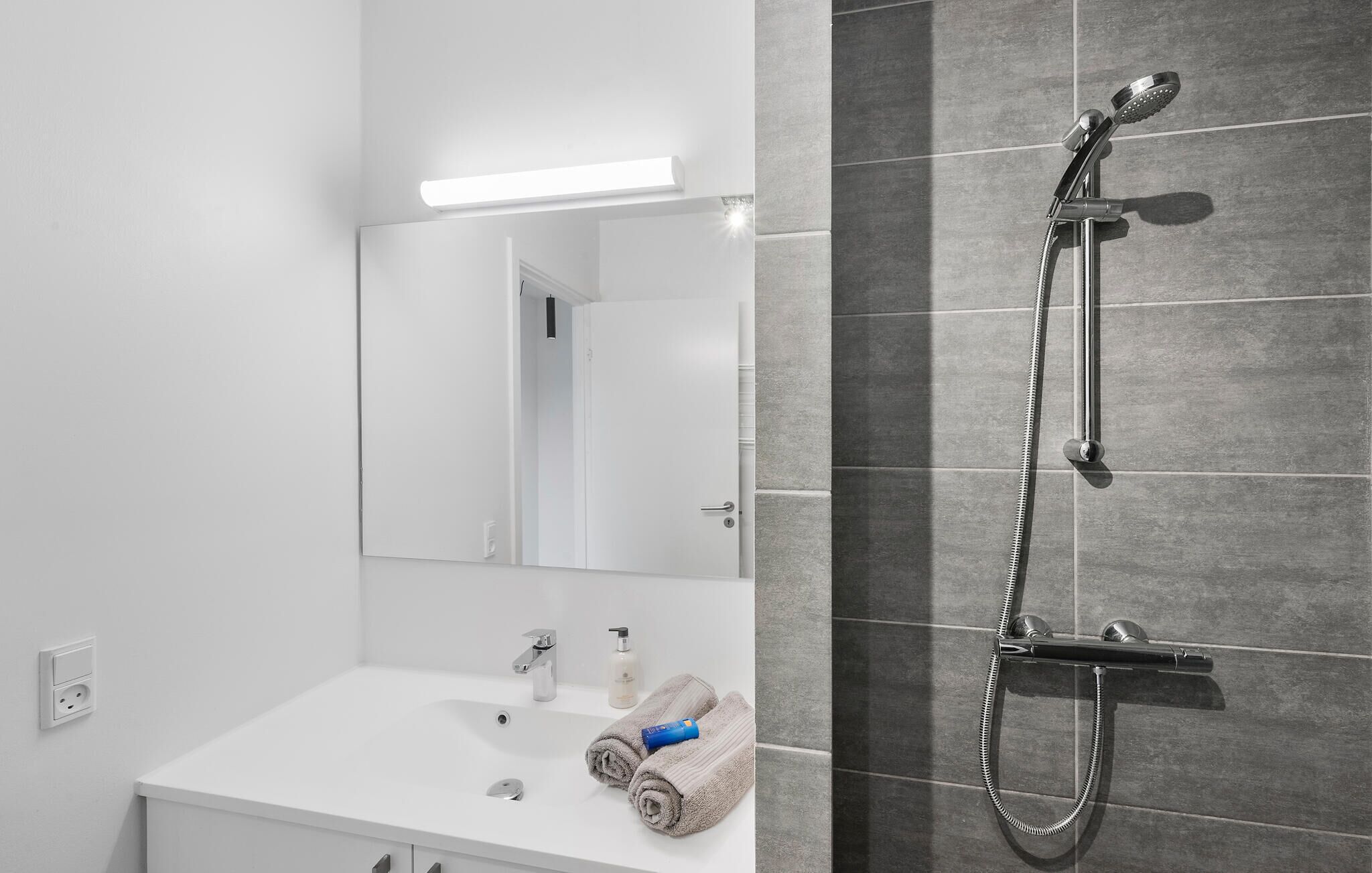 A modern bathroom with a white vanity, a mirror, a shower with a handheld showerhead, and a towel rack.
