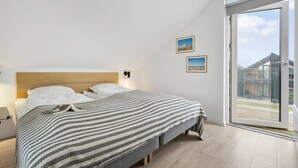 Une chambre à coucher comprenant un lit, une table de chevet, une fenêtre donnant sur des immeubles et deux tableaux encadrés accrochés au mur.