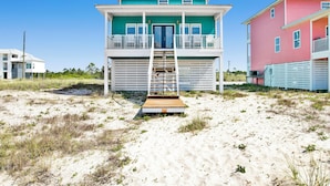 A beachfront property with a two-story building, a wooden deck, and a staircase leading to the entrance.