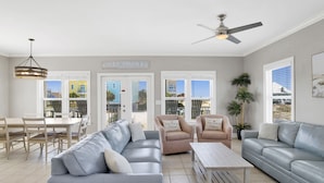 A spacious living room with a grey sofa, two armchairs, a coffee table, and a dining area with a table and chairs.