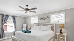 A bedroom with a bed, a ceiling fan, a nightstand with a lamp, and a window with blinds.