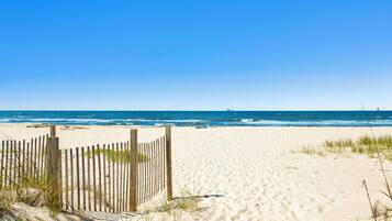 A sandy beach with a wooden fence and waves in the background.