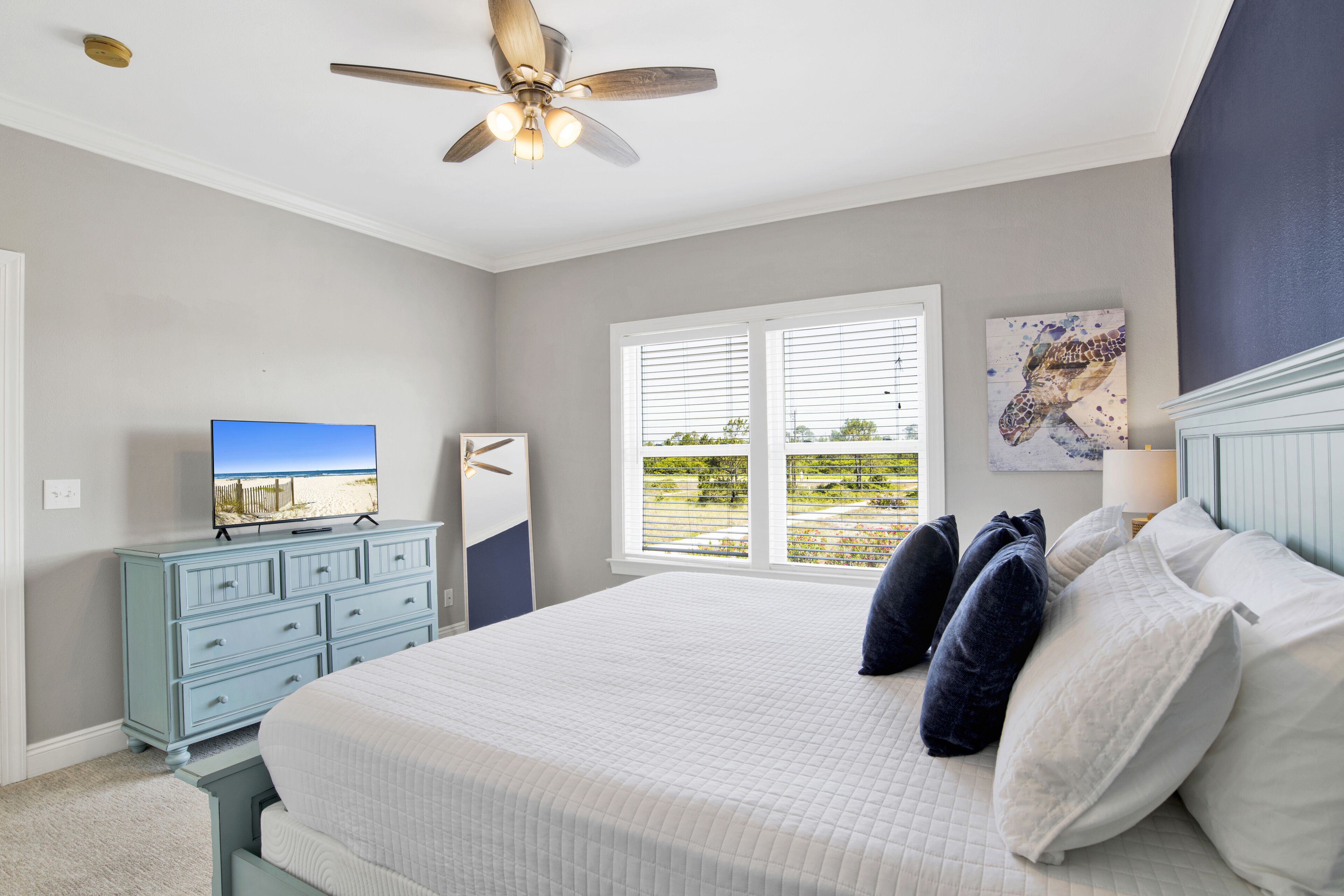 Une chambre à coucher comprenant un lit, un ventilateur de plafond, une commode et une fenêtre avec des stores.