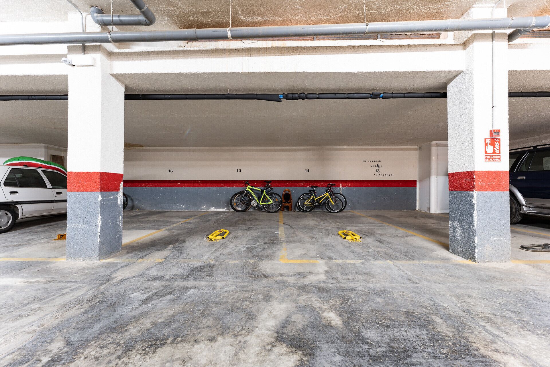 A parking garage with concrete pillars, numbered parking spaces, and a yellow caution sign on the floor.
