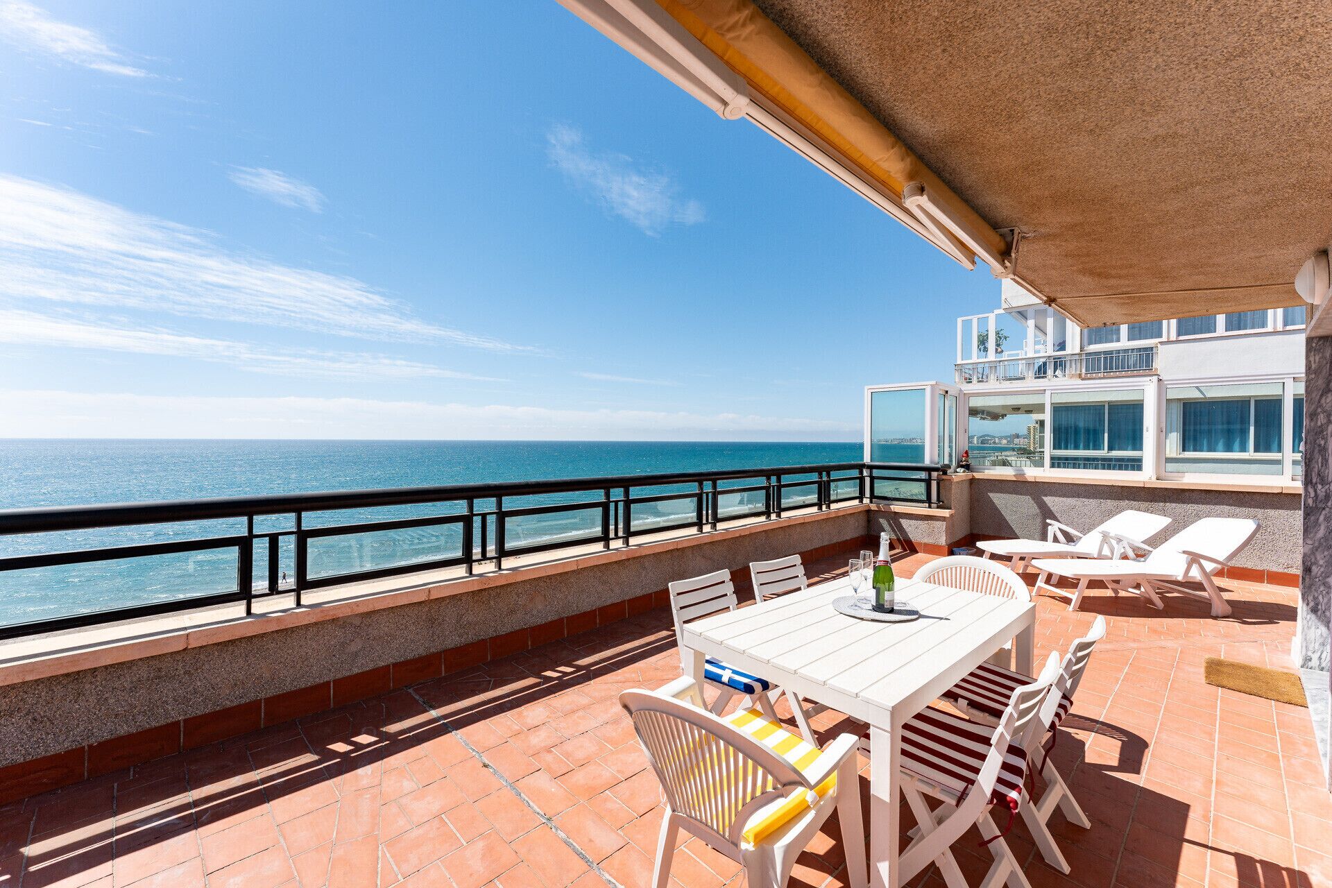 A balcony with a table and chairs, overlooking the sea.