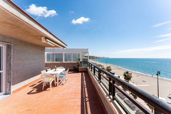 Ein Balkon mit Tisch und Stühlen mit Blick auf einen Strand und das Meer.