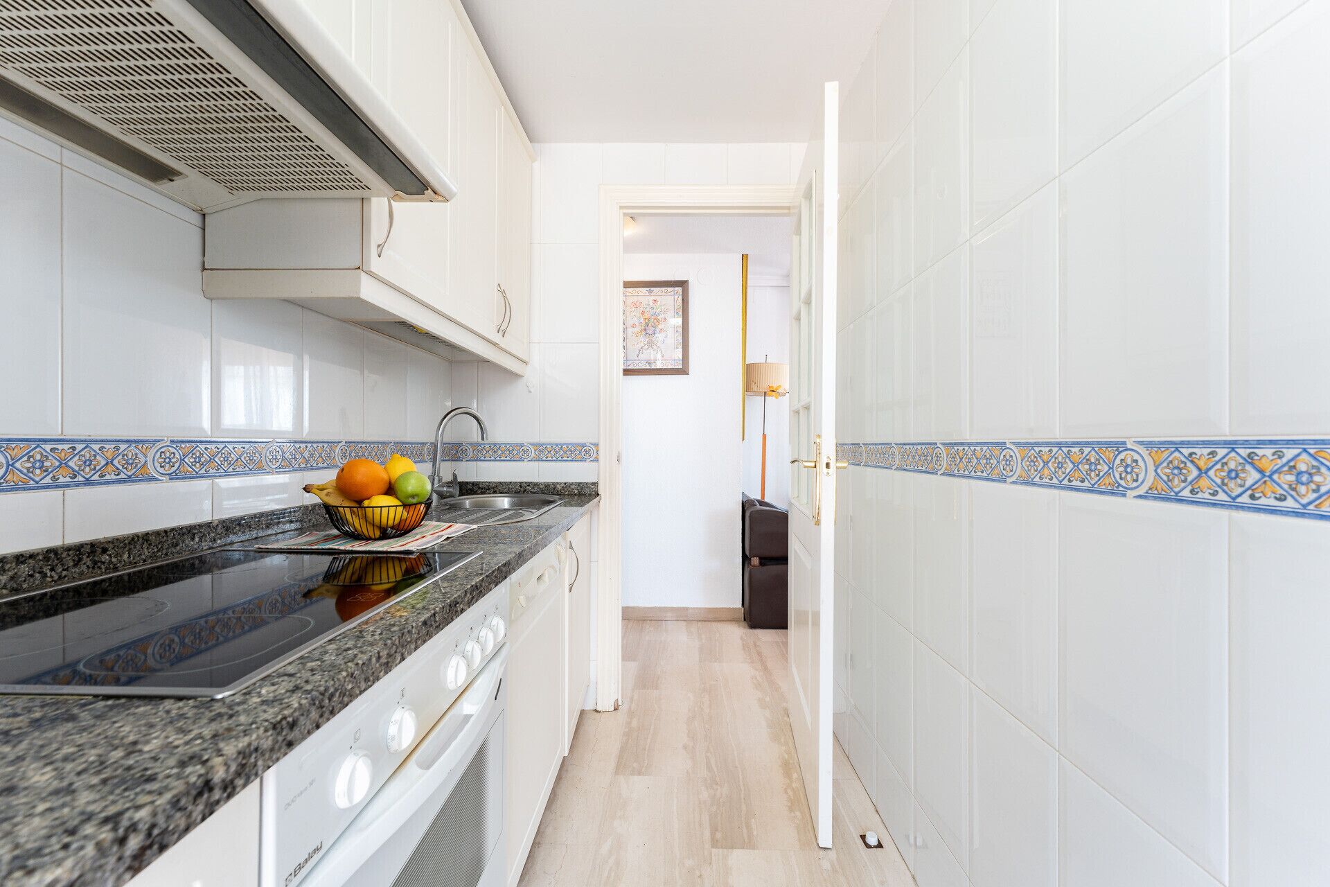 A narrow kitchen with white cabinets, a granite countertop, and a stove.