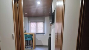 A narrow hallway with wooden doors on either side, leading to a room with a window and a table with chairs. - Casa da Capela (Ponte da barca)