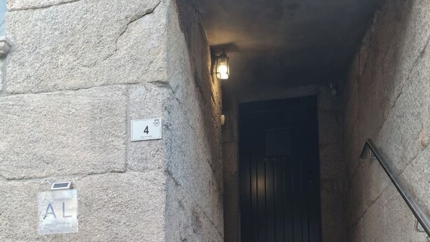 A stone building with a staircase leading to a dark door. There are signs on the wall indicating room numbers and a small outdoor area with a bench. - Casa da Capela (Ponte da barca)