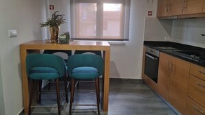 A small kitchen with a wooden table and two teal chairs, a window with blinds, and wooden cabinets. - Casa da Capela (Ponte da barca)