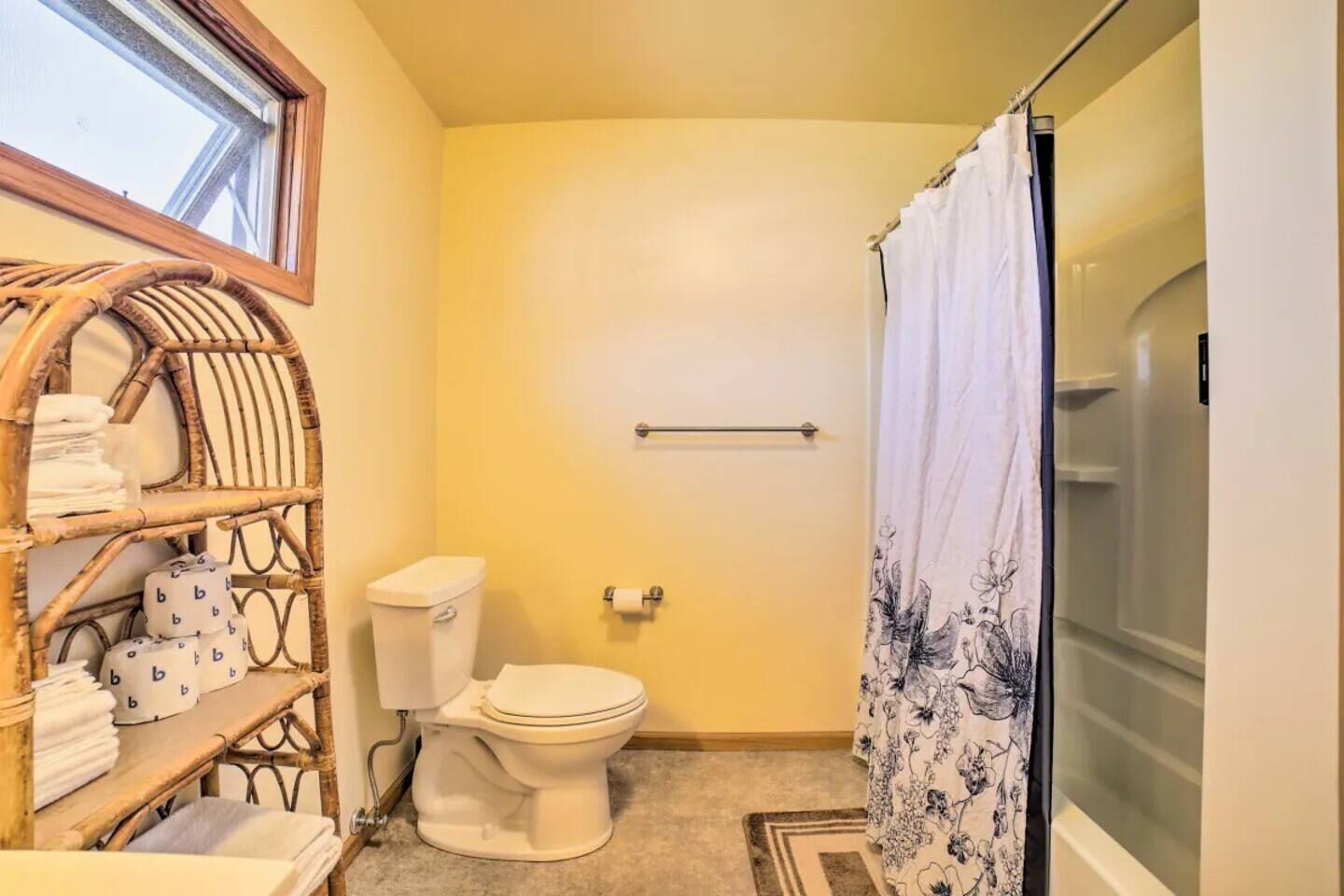 A compact bathroom with a toilet, a shower curtain, and a wicker shelf with towels.