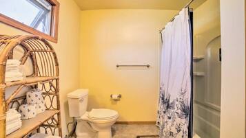 A compact bathroom with a toilet, a shower curtain, and a wicker shelf with towels.