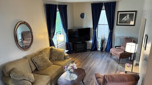 Un salon avec un canapé, un fauteuil, une télévision et une petite table ornée de fleurs.