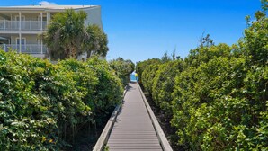 A wooden boardwalk leading to a building with balconies, surrounded by dense greenery. - Memory Lane at Magnolia Cottages (Seacrest)