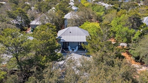 A resort with multiple buildings surrounded by dense trees, featuring a central structure with a porch and outdoor seating. - Memory Lane at Magnolia Cottages (Seacrest)