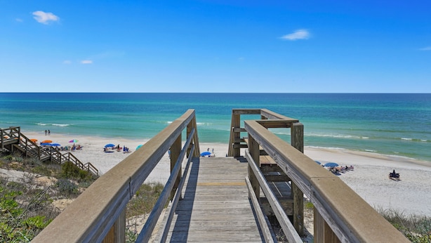 A wooden boardwalk leading to a beach with clear blue water and a few people in the distance. - Memory Lane at Magnolia Cottages (Seacrest)