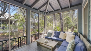 A covered outdoor seating area with a wooden table and blue cushioned sofa. - Memory Lane at Magnolia Cottages (Seacrest)