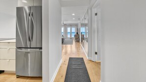 A modern kitchen with stainless steel appliances, a wooden floor, and a view of the ocean through large windows.