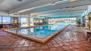An indoor swimming pool with clear blue water, surrounded by tiled flooring and equipped with a pool ladder.