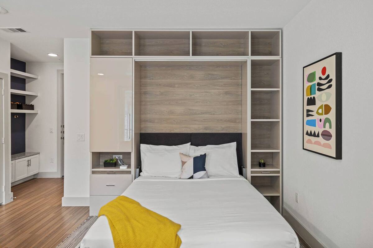 A bedroom with a bed, a nightstand, a dresser, and built-in shelving.