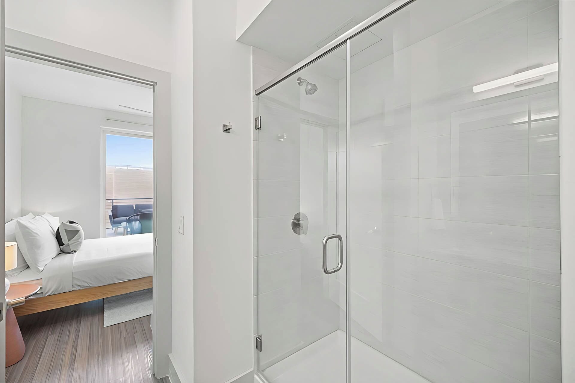 Een moderne hotelkamer met een douche in een glazen cel, een bed met witte lakens en uitzicht op het omliggende landschap.