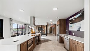 A modern kitchen with a large island, wooden cabinets, and a view to the outside. - Placemakr Austin Downtown, Apartments by Hilton (Austin)