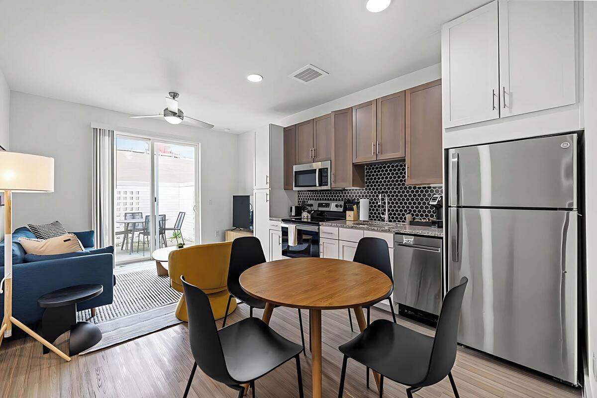 A modern kitchen with stainless steel appliances, wooden cabinets, and a dining area with a round table and chairs.
